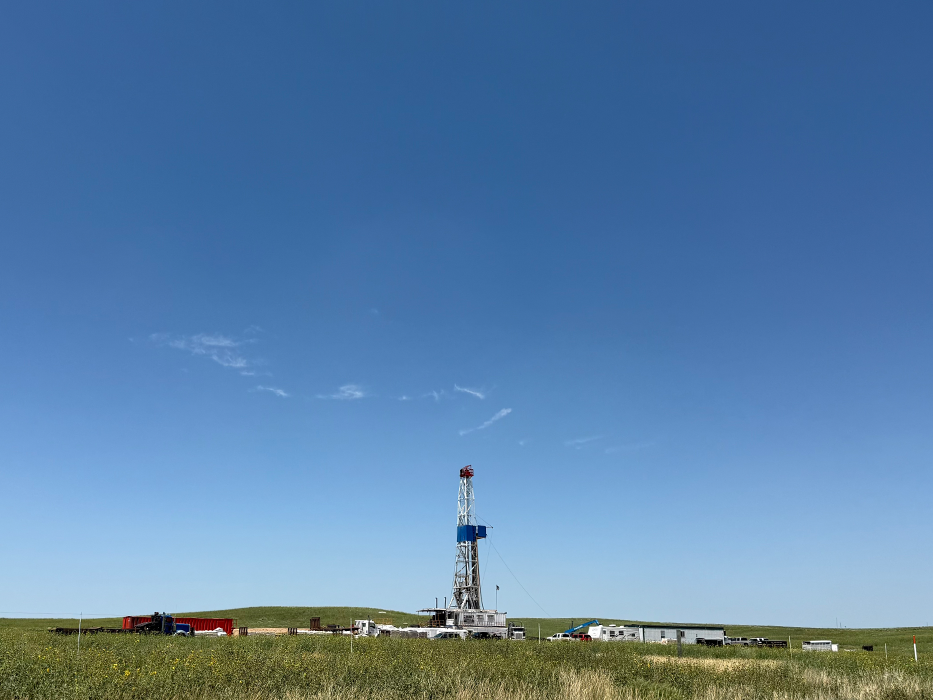 Drilling rig in operation in green field under blue sky